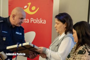 Policjant wręcza ramkę z podziękowaniami pracownikom Poczty Polskiej