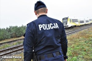 Policjant na tle przejeżdżającego pociągu.