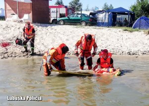 Strażacy wynoszą z wody poszkodowanego mężczyznę na desce ratowniczej.