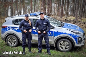 Policjanci stojący przy policyjnym radiowozie w lesie.