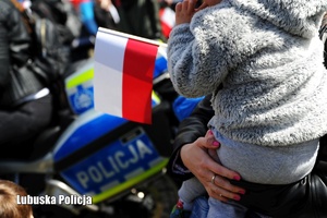 Dziecko trzymające flagę Polski, a w tle policyjny motocykl.