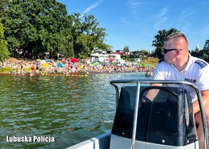 Policjant podczas patrolu na jeziorze - w tle osoby kąpiące się.