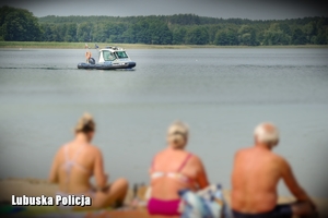 Plażowicze na brzegu, a w tle policjanci patrolujący jezioro na motorówce.