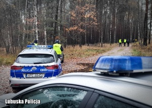 Policyjne radiowozy, a w tle policjanci podczas ćwiczeń sztabowych w lesie.