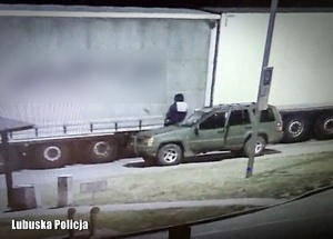 Ciężarówka na parkingu, a obok niej mężczyzna stojący przy samochodzie.