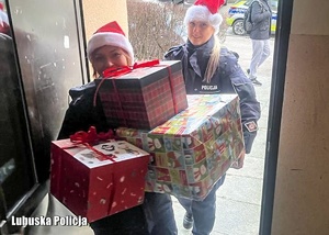 Policjantka w czapkach Świętego Mikołaja wchodzą do budynku z prezentami świątecznymi.