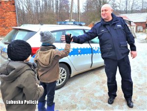 Policjant przy radiowozie witający się z dziećmi.