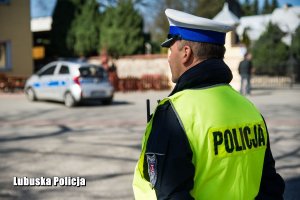 Policjant drogówki, a w tle policyjny radiowóz.