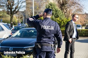 Policjant obok mężczyzny w garniturze i zaparkowanego pojazdu osobowego.