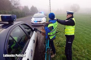 Policjant ubiera w kamizelkę odblaskową rowerzystkę.