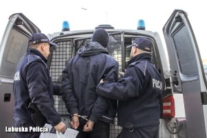 Policjanci z zatrzymanym mężczyzną przy radiowozie.