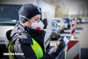 Policjantka w maseczce ochronnej, a w tle pojazdy osobowe.