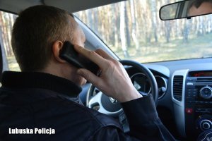 Policjant rozmawiający przez telefon komórkowy w radiowozie.