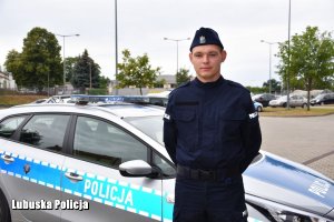 młody policjant stoi przed radiowozem