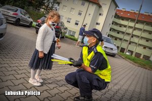 Policjanta przy małej dziewczynce, której przekazuje element odblaskowy.