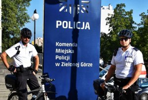 Policjanci z patrolu rowerowego przy logo Komendy Miejskiej Policji w Zielonej Górze
