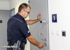 policjant zamyka drzwi  od pomieszczenia dla osób zatrzymanych.