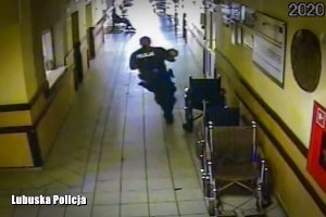 Policjant z dzieckiem na rękach biegnie po szpitalnym korytarzu