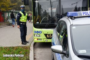 Umundurowany policjant przy autobusie komunikacji miejskiej.