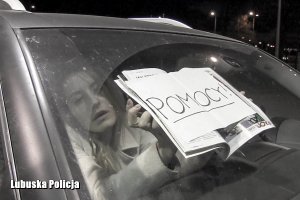 kobieta w samochodzie przykłada do szyby kartkę z napisem POMOCY