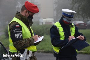 Żandarm i policjant podczas uzupełniania notatników służbowych.