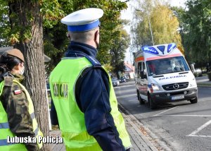 Policjant ruchu drogowego i żołnierka patrzą na abmulans pogotowia ratunkowego