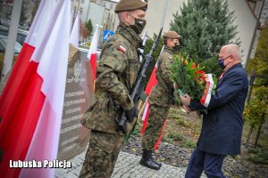 Wojewoda Lubuski składa kwiaty przy pomniku - obok niego żołnierze.