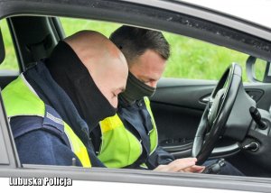 Policjanci w radiowozie przeglądają dokumenty i sprawdzają kierowcę w bazach danych