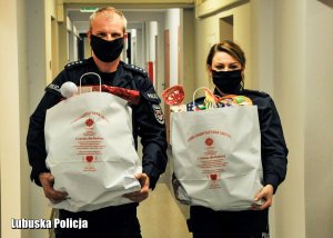 Policjant i policjantka przy zbiórce produktów dla potrzebujących. Niosą torby.