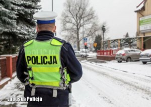 Policjant na chodniku - w tle droga pokryta śniegiem.