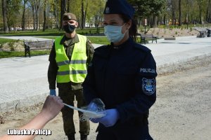 Policjantka i żołnierz rozdają maseczki.