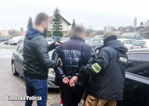 Policjanci kryminalni prowadzą zatrzymanego do radiowozu nieoznakowanego