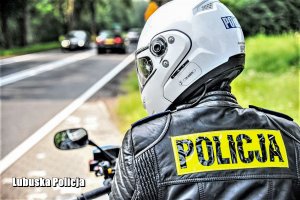 Policyjny motocyklista w kasku ochronnym, a w tle droga.