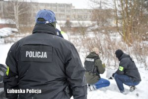Policjanci śledczy i operacyjni w kamizelkach wraz z technikiem kryminalistyki przy oględzinach