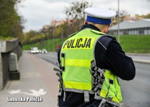 Policjant ruchu drogowego stojący tyłem. Mierzy prędkość kierowców