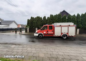 Pojazd straży pożarnej na jednej ulic, a obok strażacy.