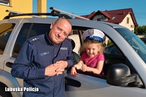 Policjant z dzieckiem, które siedzi w radiowozie.