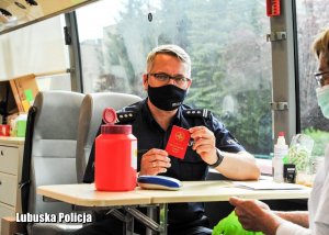 Zastępca Komendanta Wojewódzkiego Policji pokazujący  legitymacje honorowego dawcy krwi