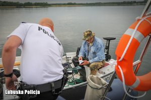 Policjant na policyjnej łodzi. W tle wędkarz na łódce