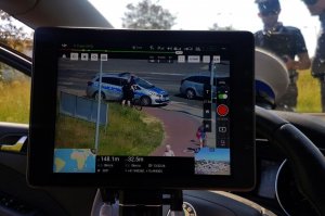 Policjant kontroluje i obserwuje na wyświetlaczu pracę drona. Widoczna kontrola rowerzysty