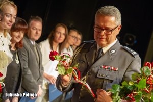 Zastępca Komendanta Wojewódzkiego Policji w Gorzowie Wielkopolskim  z kwiatem. W tle kobiety