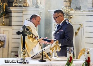 Zastępca Komendanta Wojewódzkiego Policji w Gorzowie Wielkopolskim przekazuje dokument osobie duchownej przy ołtarzu