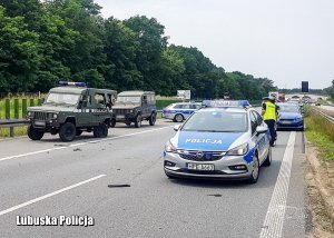 Policyjny radiowóz oraz pojazdy wojskowe na drodze.