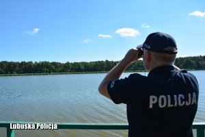 Policjant nad jeziorem spogląda przez lornetkę.