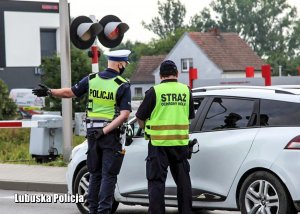 Policjant i funkcjonariusz Straży Ochrony Kolei przy samochodzie osobowym.