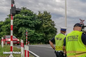 policjant i funkcjonariusz Straży Ochrony Kolei obserwują ruch na przejeździe kolejowym