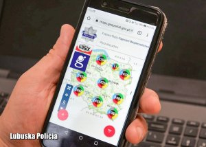 Telefon komórkowy z widoczną mapą Polski w dłoni - w tle klawiatura od komputera.