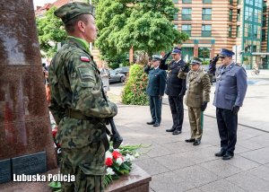 Przedstawiciele służb mundurowych składają kwiaty pod pomnikiem.