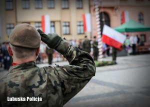 Żołnierz oddający honor, a w tle flaga Polski.
