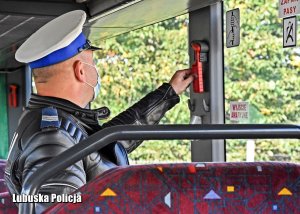 Policjant w autobusie sprawdza przyrząd do wybicia szyby.